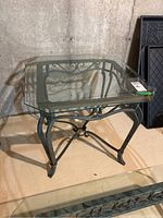 Full view of the side table showing square beveled glass top and decorative metal base.