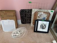 Photo showing storage rack box, fabric and metal grid note boards, wrapped miscellaneous parts, and framed and unframed wall photos leaning against a pink wall.