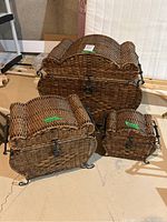 Three wicker baskets with metal trim and curved lids arranged on a floor, showing the set together.