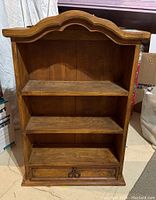 Front view of wooden shelf unit showing two shelves and bottom drawer with metal pulls
