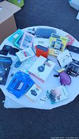 Photo of entire lot showing Beats headphones box, Kindle covers in packaging, iHome speaker, Brookstone charger and assorted electronic accessories on white table.