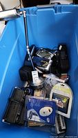 Blue plastic bin containing various electronic items including a lamp, cables, batteries, and electronic devices.