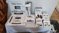 Overview of all boxed items on table including Village Streetcar, Autumn Trees, and Market Day figurines