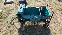 Folding wagon showing green fabric divided interior with black metal frame and wheels on grass.