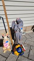 Full view of the outdoor bunny statue, angel statue, and ceramic vase displayed on pavement with measuring stick for height reference
