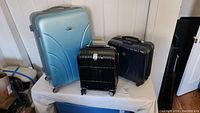 Three luggage pieces arranged on a table: large blue suitcase at back left, small black suitcase front center, medium navy suitcase back right.