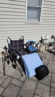 Wide view of wheelchair, walkers, and wedge pillow outdoors against building wall