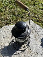Photo showing black metal lantern with wooden handle resting on stone outside in natural light.