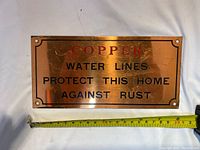 Front view of the antique copper sign with text and a measuring tape showing approximately 12 inches in length.
