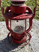 Front view of the antique red Dietz railway lantern showing glass globe with Dietz New York embossed marking and wire cage.