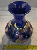 Front side view showing flared opening and floral hand-painted design on bulbous body with measuring tape indicating size.