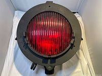 Front view of the antique railway light showing the red ribbed glass lens secured by metal clips in black metal housing.