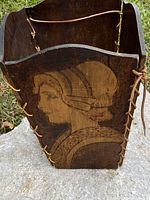 Top edge and side profile with woman's face wood burned into the wood showing details of the laced leather cord binding and carved lines.