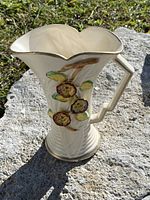 Front and side view of the cream-colored ceramic pitcher with floral raised decoration and a wavy rim