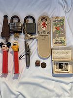 Overview of assorted collectibles including locks, PEZ dispensers, shoehorn, lottery tickets, badges, coin, and small photo box.