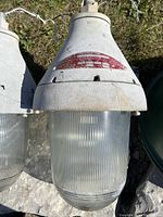 Close-up photo of the metal top and ribbed glass globe of one light, showing weathering and manufacturer label with details.