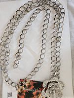 Full view of the Nobia chrome chain belt showing linked rings and jeweled rose buckle with attached tag.
