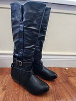 Photo showing full view of the tall black boots with side zipper, ankle straps, and buckle detail.