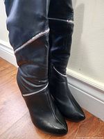 Front and side view of black women's boots with decorative silver zippers, pointed toe, and visible slight wear.
