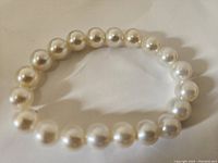 Close-up of faux pearl bracelet showing round beads with smooth and glossy finish, elastic string visible between beads.