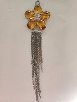 Front view of gold tone flower pendant with amber glass petals, clear rhinestone center, and silver chain tassels.