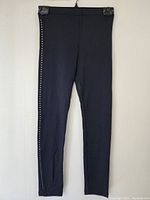 Front view of black ladies decorative tights with studs hung on plastic hanger, showing full length and decorative elements.