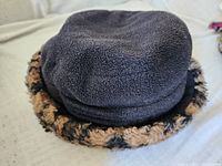 Black fleece hat with leopard print faux fur trim on a beige surface.
