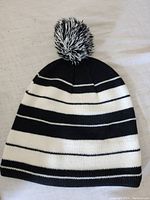 Front view of black and white striped knit hat with pom pom on top showing shape and pattern