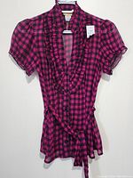 Front view of the pink and black checkered ladies top showing the ruffled details and belted waist.