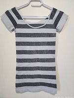 Front view of ladies short-sleeve top with black and gray horizontal stripes, hung on hanger against a wall.