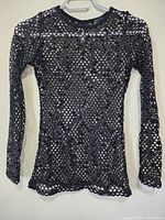 Front view of metallic black ladies top with decorative cut-out pattern hung on hanger