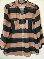 Front view of the ladies decorative top showing bold horizontal black and beige stripes, button closure, collarless neckline, and chest pockets.