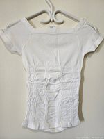 Full front view of the white short sleeve ladies top showing the overall shape, neckline, and ruched fabric details.