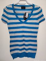 Photo front view of LaVOCA ladies top hanging on a hanger showing blue and light gray stripes, V-neck and short sleeves.