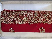 Front view of the rectangular red purse showing intricate hand sewn jewels and gold embroidery on the flap.