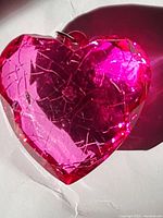 Close-up photo of a pink rose glass heart pendant with diamond cut facets and small metal loop.