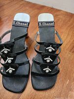 View of pair of black S.Chanel strappy sandals with jeweled embellishments and square open toe on wood floor