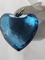 Close-up of heart-shaped teal glass pendant showing facet reflections and gold-tone bail