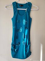 Full view of turquoise sleeveless top on hanger, laid flat on wall, showing shape and length