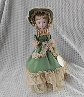 Full view of the doll showing the green dress with beige lace trim and flared skirt.