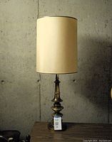 Front view of the full lamp showing the tall brass base with decorative stacked shapes and the beige fabric shade.