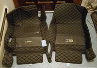 Photo of two front car floor mats, black quilted design with Chitu logo patches, showing raised edges and cutouts.