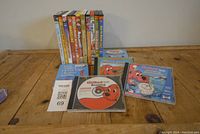 Photo of children's DVDs and Scholastic Clifford The Big Red Dog CDs arranged on a wooden surface, showing colorful covers and disc art for identification.