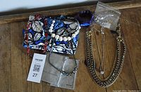 Overview photo showing mixed costume jewelry including necklaces, bracelets, rings, a blue Vera Bradley fabric jewelry keeper with butterfly design, and two gray David Yurman pouches on a wooden surface.