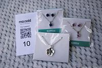 Three packaged jewelry sets including blue earrings with blue pendant, pink earrings with pink pendant, and silver flower pendant necklace.