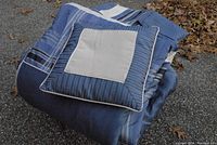Folded blue reversible king size comforter topped with a pillow featuring blue stripes and cream panel.