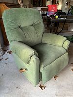 View of green La-Z-Boy recliner chair showing front angle with manual recline lever visible on side. Fabric upholstery appears worn with some dirt.