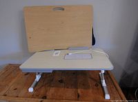 Front view of the lap desk showing beige surface with adjustable white legs and handle cutout.