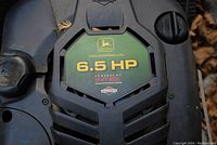 Close-up of the engine label showing 6.5 HP Briggs and Stratton Intek branding and John Deere logo.