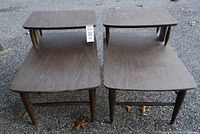 Front view of the pair of mid-century modern wooden end tables showing tops and lower shelves, with surface wear visible.